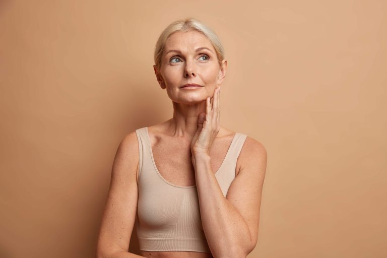 woman-touches-skin-after-applying-anti-age-cream-concentrated-with-thoughtful-expression-wears-cropped-top-isolated-brown (1) (1)